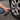Close-up of a person kneeling on asphalt while inflating a car tire using a black portable cordless tire inflator with a digital pressure gauge display.